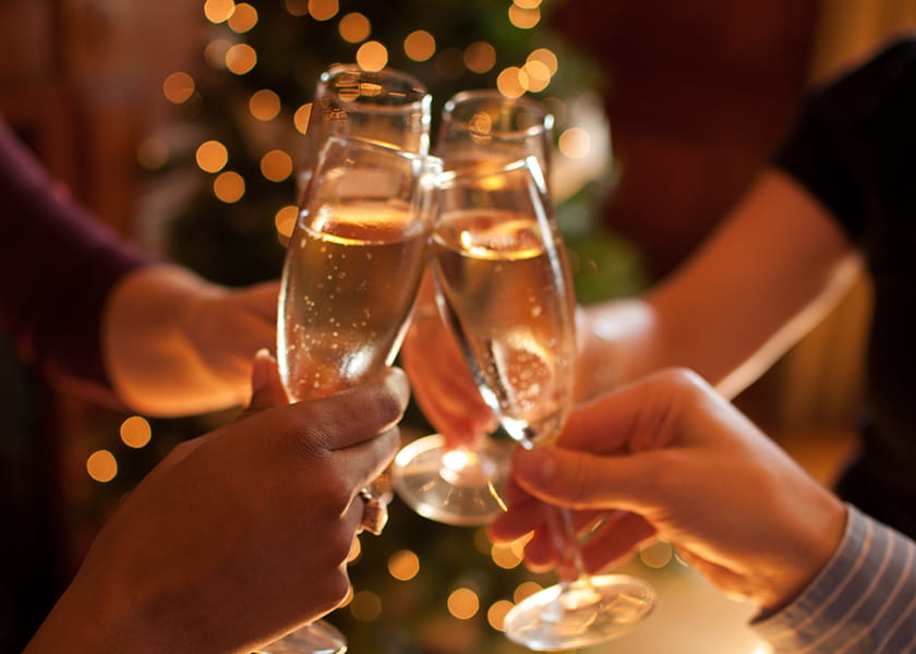 Close-up of four people clinking champagne flutes together in a toast against a warm, blurred bokeh light background.